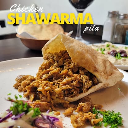 Chicken shawarma pita filled with seasoned grilled chicken, garnished with fresh herbs and served with a side salad.