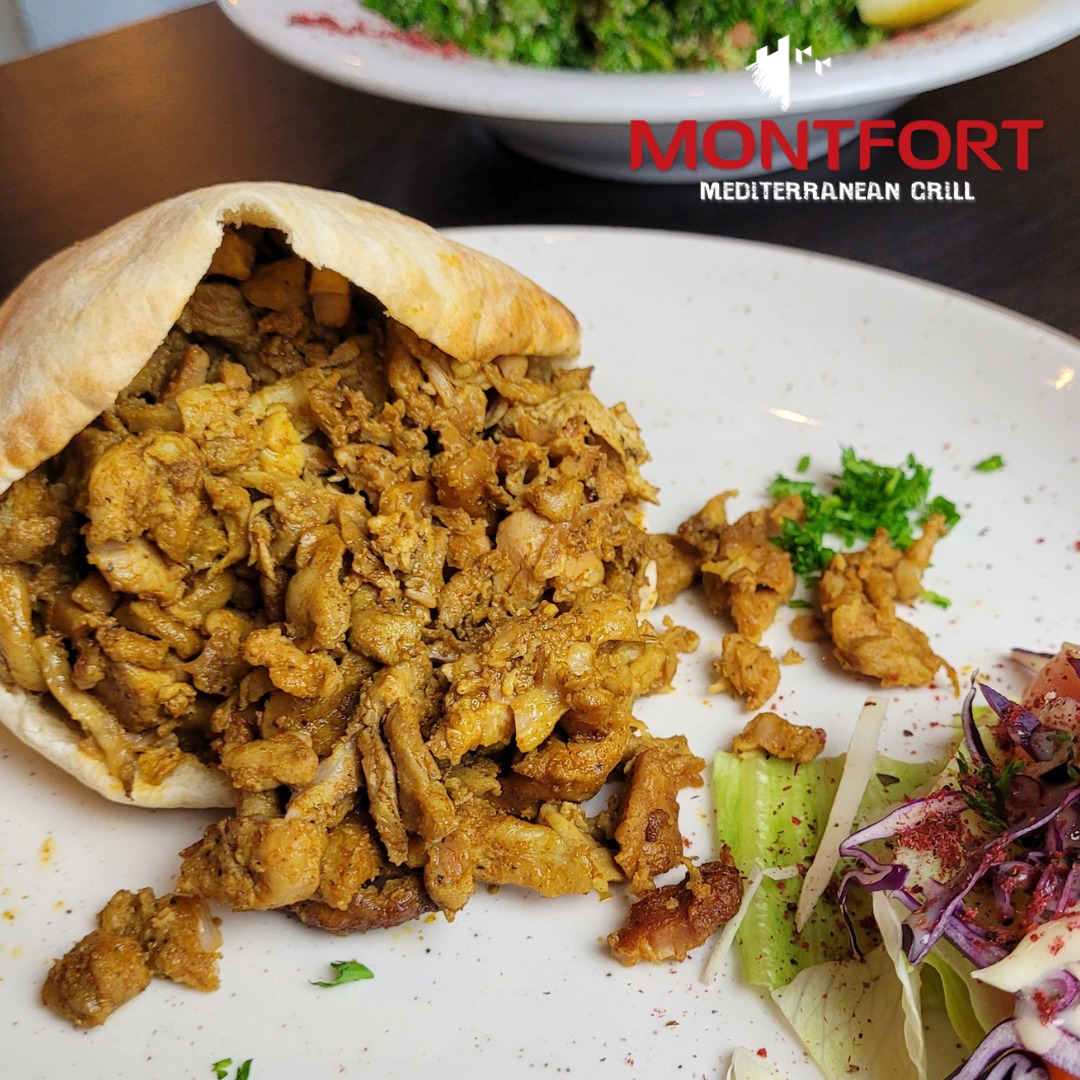 Seasoned chicken shawarma spilling out of pita bread on a white plate with a side of fresh salad greens.