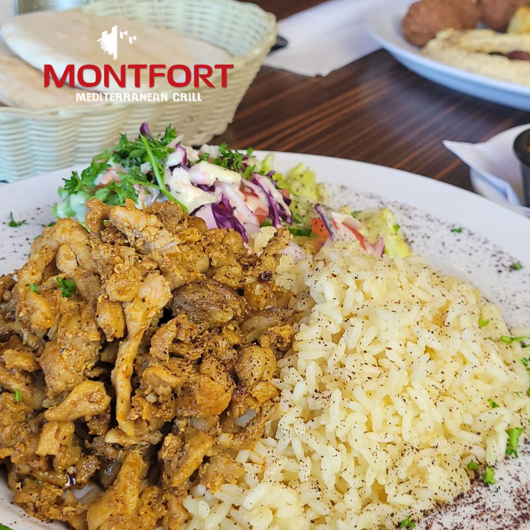 Plate with seasoned grilled chicken, white rice with black pepper, and mixed salad with creamy dressing on a wooden table.