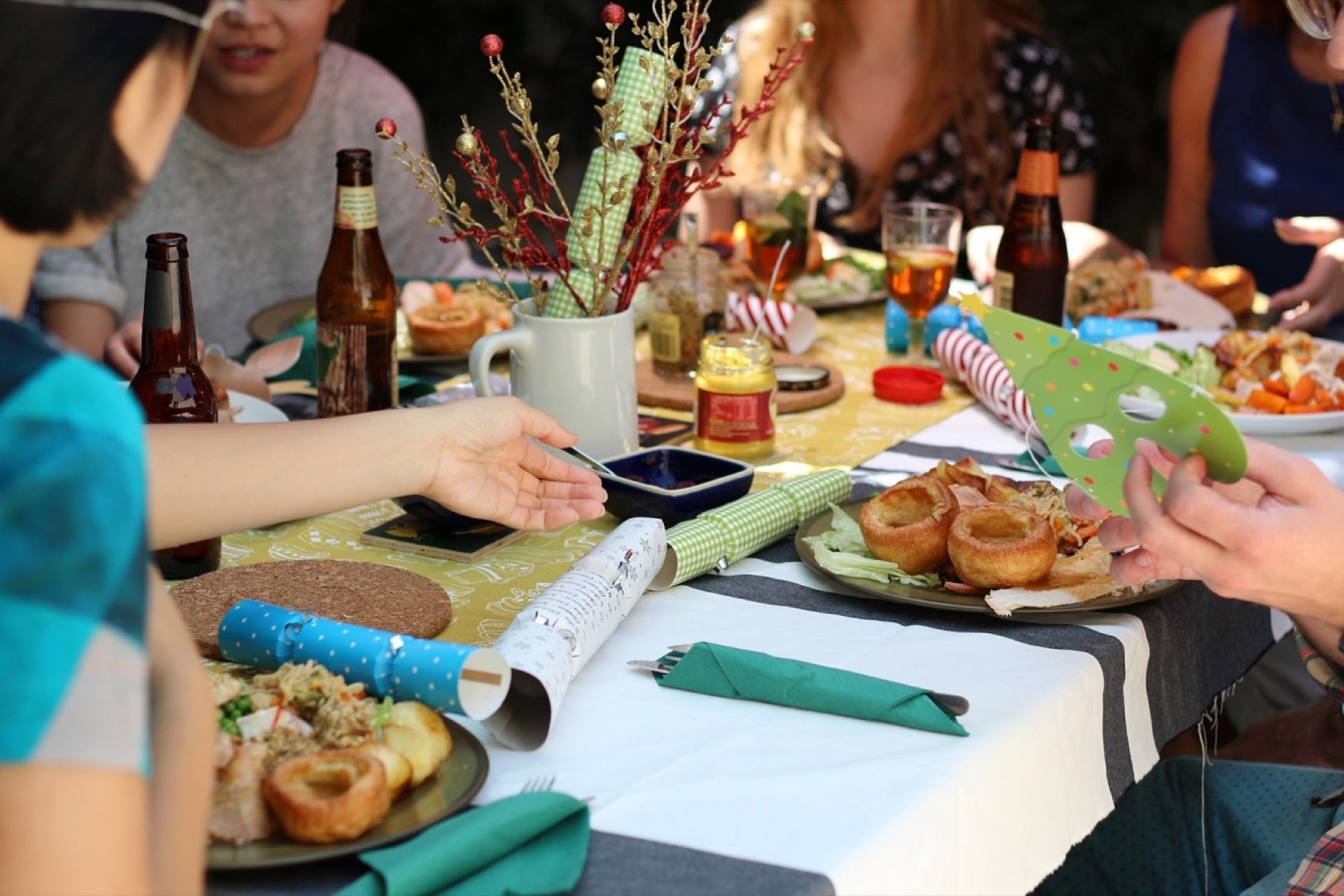 People gathered around a festive table with plates of food, drinks, Christmas crackers, and holiday decorations.