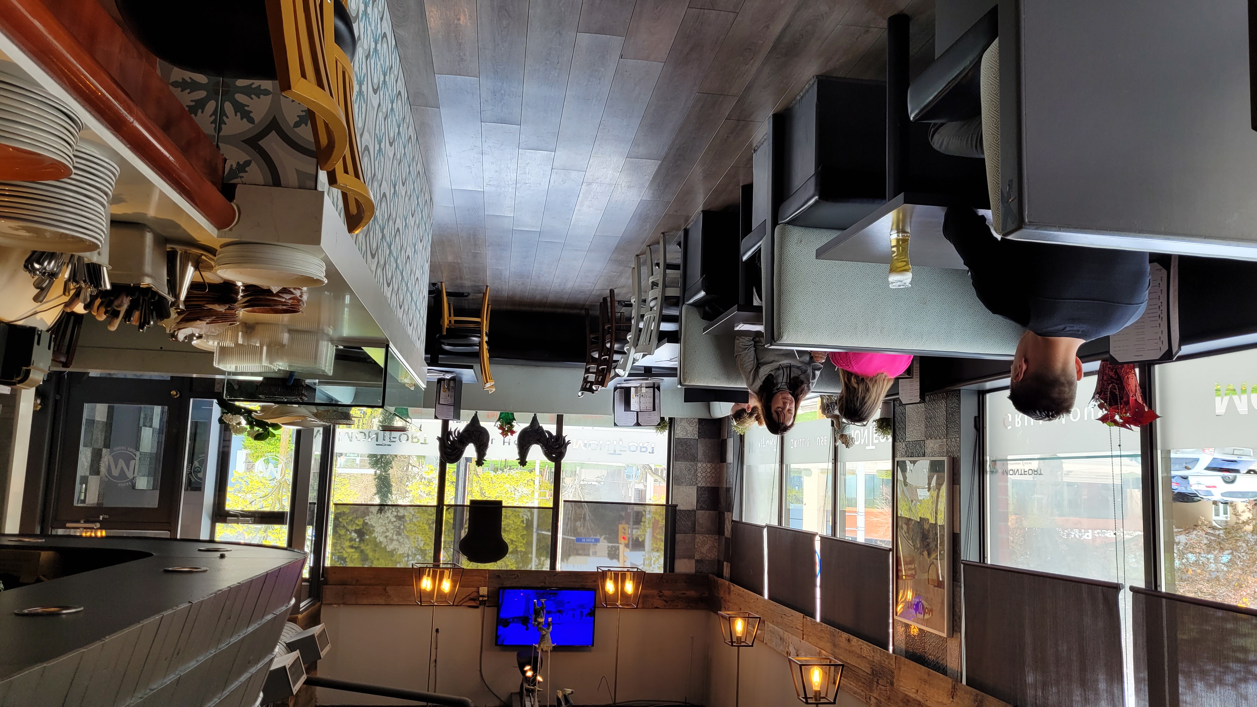 Interior of a cozy restaurant with wooden floors, several booths and tables, and a bar counter with stacked plates and utensils.