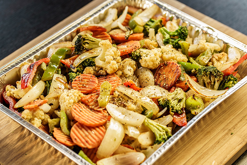 Tray of seasoned roasted mixed vegetables including carrots, cauliflower, broccoli, onions, and bell peppers.